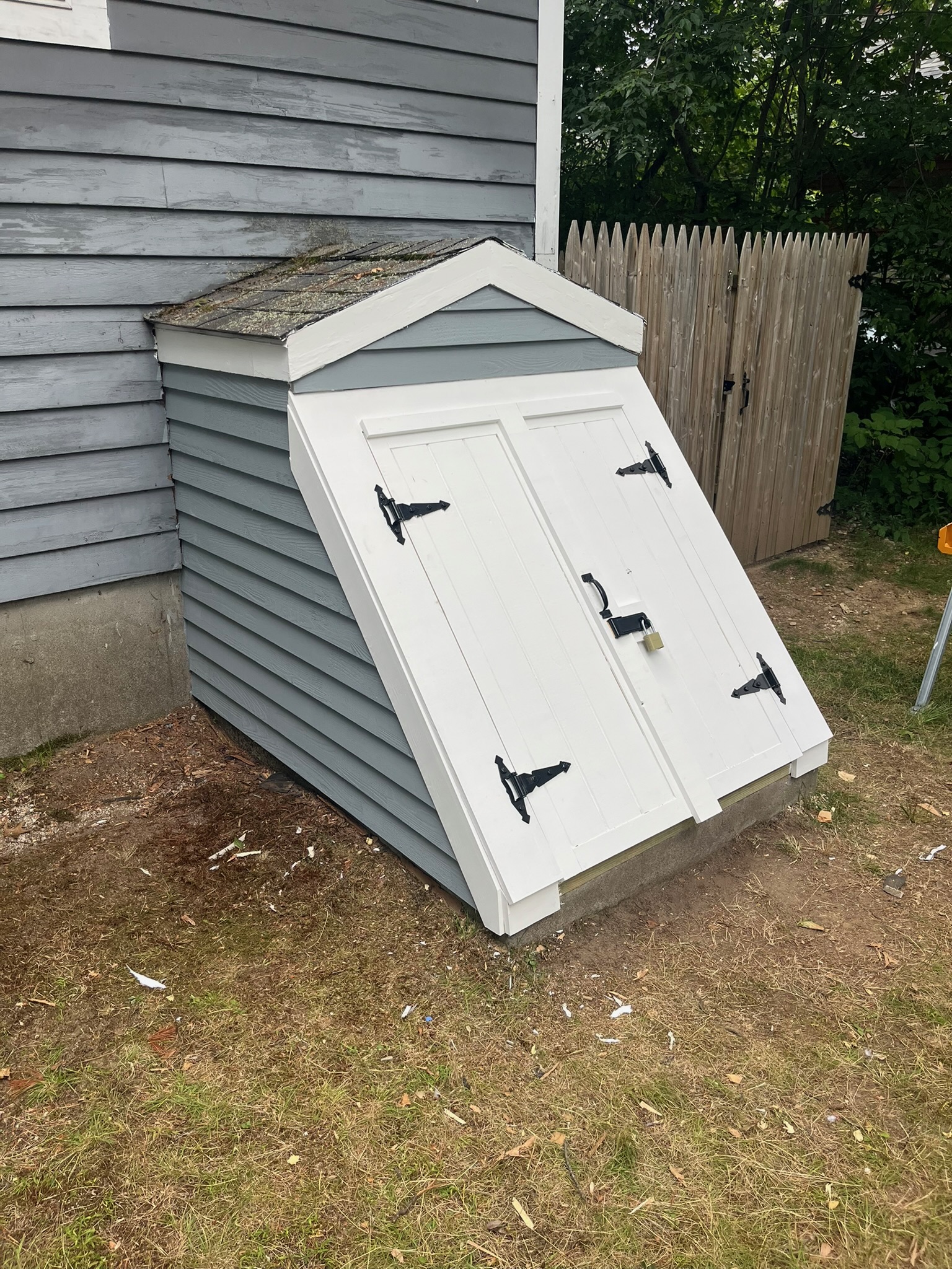 White bulkhead-style storage shed built against the side of a house