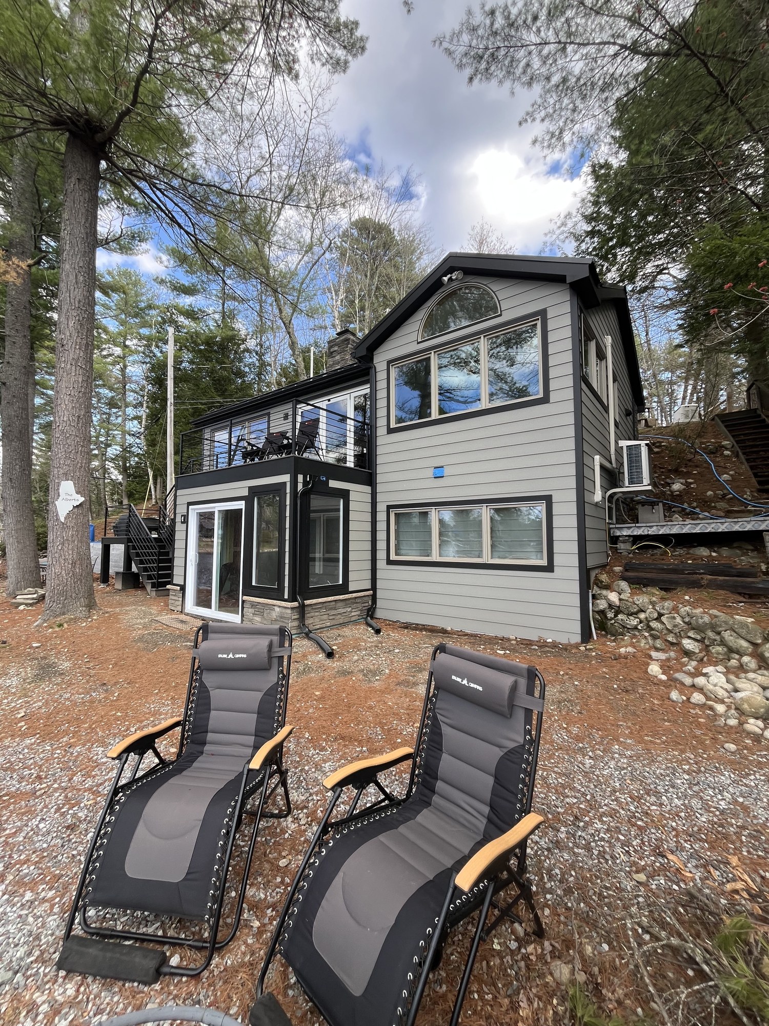 Finished waterfront home with gray siding, black trim, and lounge chairs looking back at the house